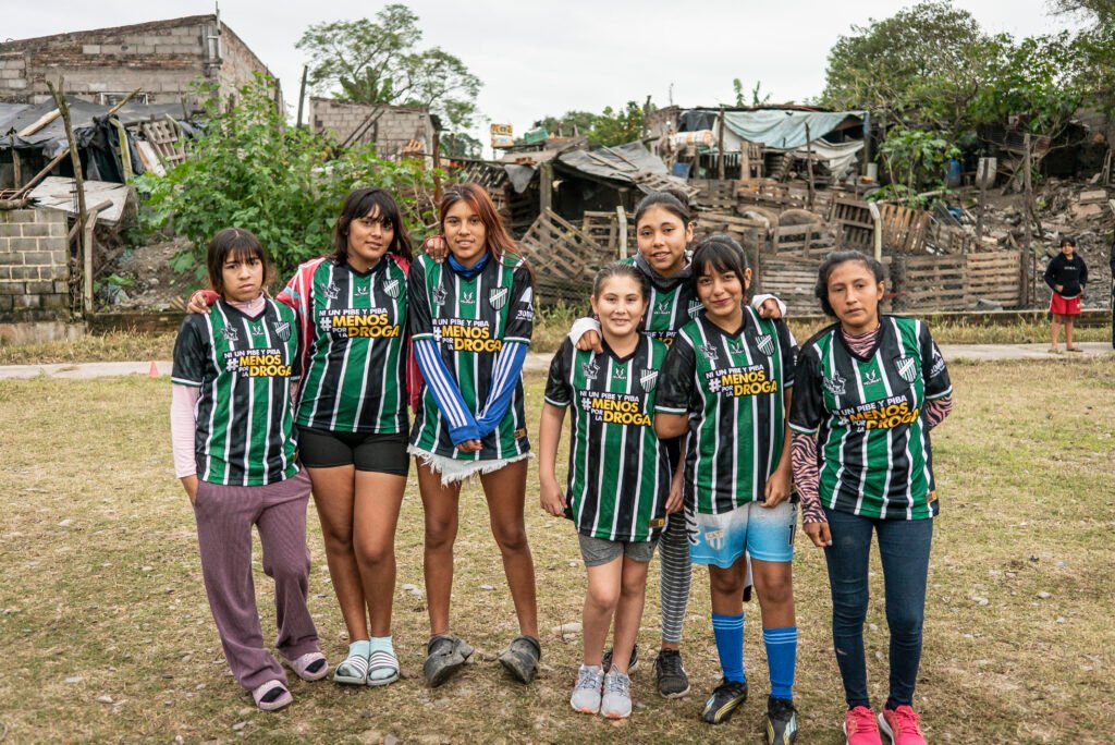 Este imagen muestra a una joven con cabello largo oscuro recogido en una cola de caballo con un coletero azul, vistiendo una camiseta de fútbol negra y verde a rayas.