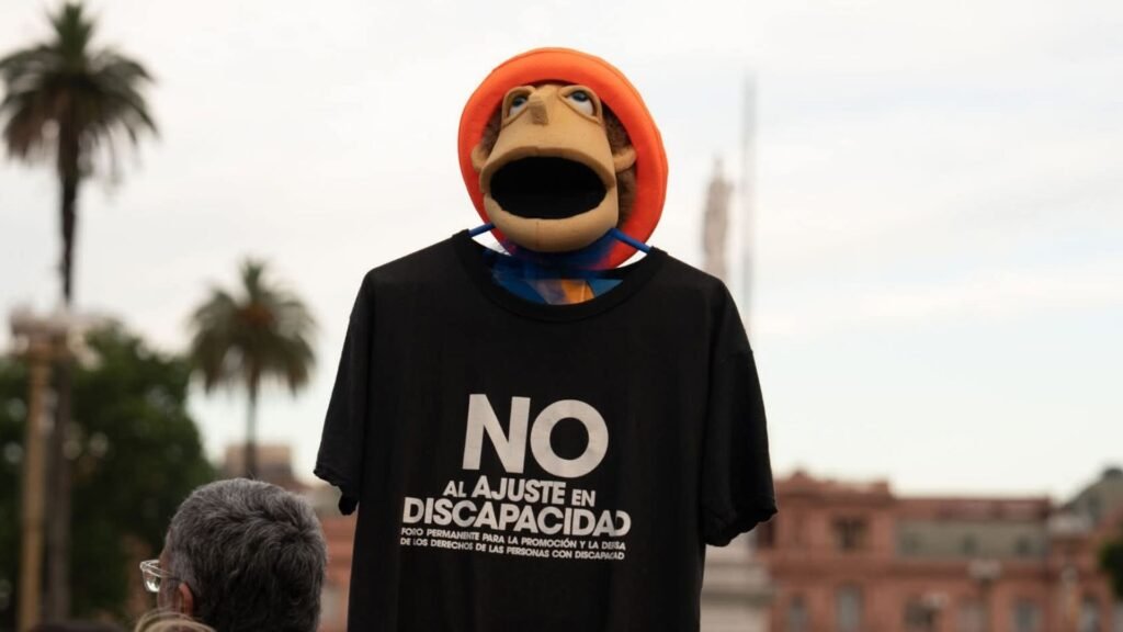 Un muñeco de gomaespuma hoy es el faro de las marchas contra el ajuste en discapacidad. Luego de la partida de su creador, tomó las calles con la remera de la lucha para ser la presencia física y el grito de todos aquellos que no pueden viajar a las plazas pero exigen ser reconocidos.
