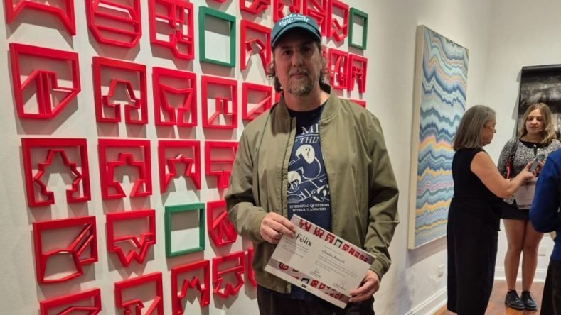 El artista visual Claudio Roncoli aparece en la imagen sosteniendo el diploma de reconocimiento por su obra “No soy feliz pero vivo cerca de un Mc Donald”, la cual fue seleccionada en la 55ª edición del Salón de Artes Visuales Fernán Félix de Amador (“El Félix”) en la Quinta Trabucco, ubicada en Vicente López, Buenos Aires.