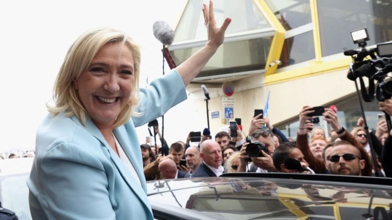 Esta imagen muestra a la política francesa Marine Le Pen saludando alegremente a una multitud de seguidores durante un acto de campaña electoral.