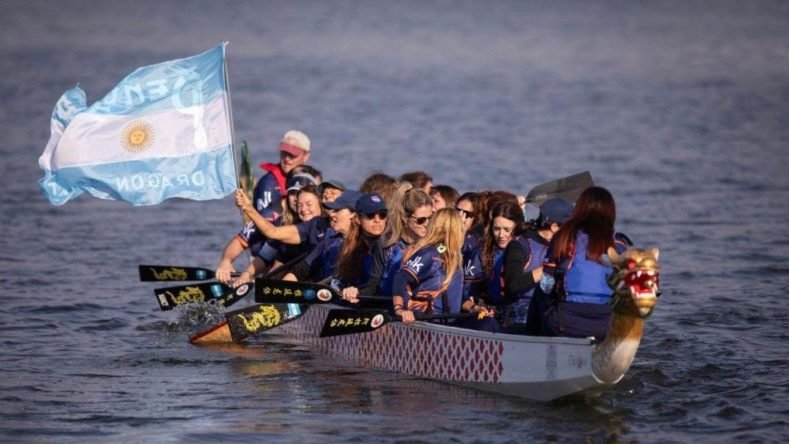 Este equipo participa en una carrera de botes dragón tradicionales chinos organizada en Argentina, luciendo chalecos salvavidas azules sobre camisetas deportivas