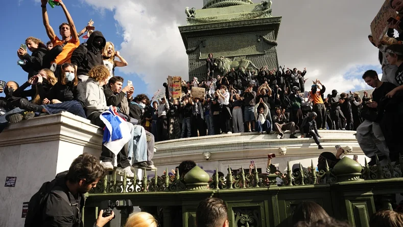 La imagen muestra a manifestantes subidos a la base del monumento en la Plaza de la Bastilla en París, Francia, durante las masivas protestas estudiantiles y movilizaciones sociales de octubre de 2026 contra la crisis educativa y el alto costo de vida.
