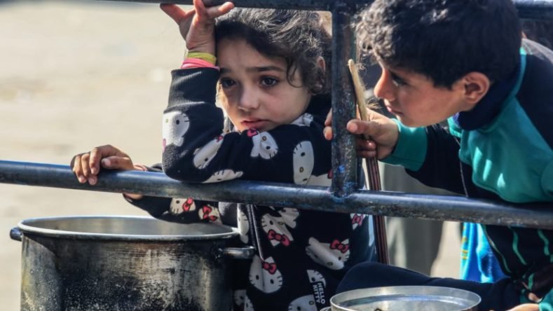 Esta imagen muestra a niños en un campo de refugiados en Rafah, Gaza, esperando alimentos durante la crisis de hambruna.