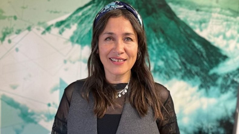 Esta imagen muestra a una mujer sonriendo frente a un mural con tonos verdes y blancos.