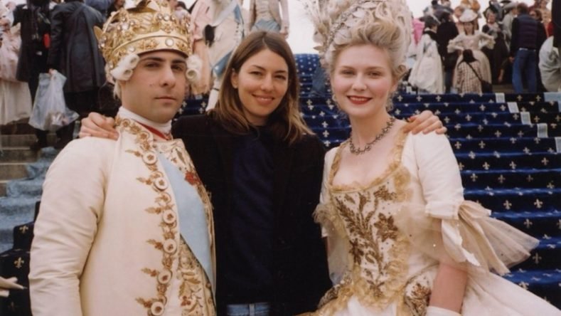 La imagen muestra a la directora Sofia Coppola en el centro, acompañada por los actores Jason Schwartzman (como el rey Luis XVI) y Kirsten Dunst (como María Antonieta) durante el rodaje de la película María Antonieta (2006) en el Palacio de Versalles.