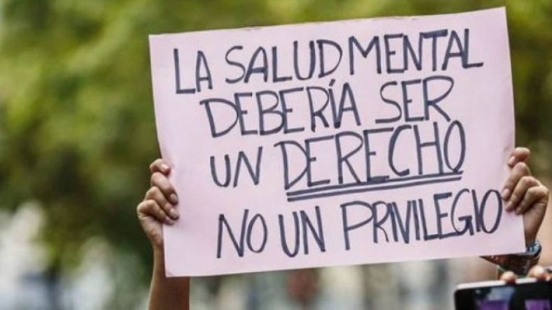 La imagen muestra un cartel de protesta rosado que dice "La salud mental debería ser un derecho, no un privilegio" en el marco de los debates actuales sobre la legislación y las políticas sanitarias.