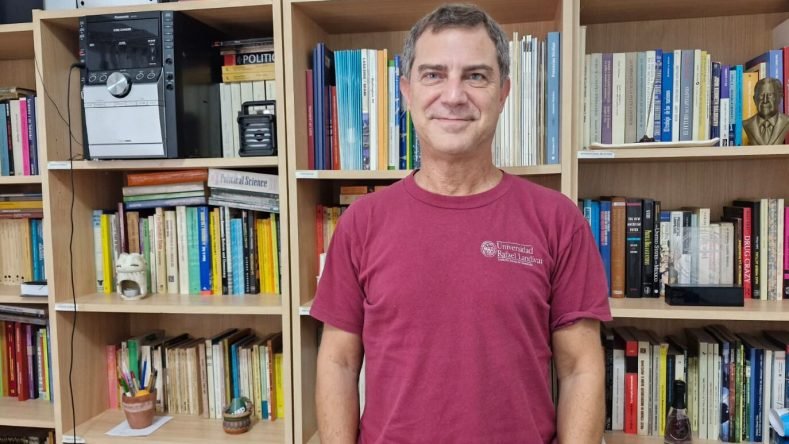 Esta imagen muestra a una persona frente a estanterías llenas de libros, vistiendo una camiseta roja de la Universidad Rafael Landívar.