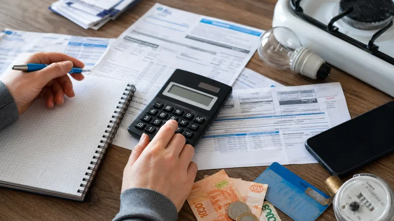 La imagen muestra a una persona organizando y calculando el pago de sus facturas y servicios del hogar.