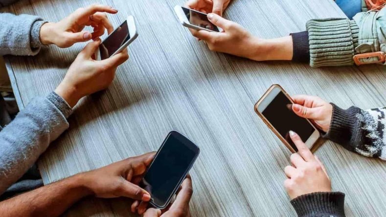 Esta escena representa un fenómeno común donde las personas utilizan sus dispositivos móviles durante interacciones sociales, lo cual puede generar discusiones o afectar la calidad de las relaciones personales.