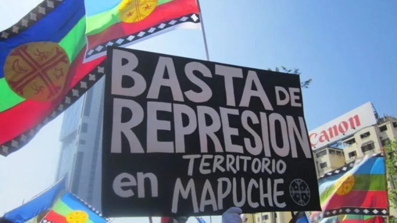 El cartel en la imagen muestra la consigna «BASTA DE REPRESIÓN en territorio MAPUCHE», acompañado de banderas del pueblo mapuche (wenufoye).