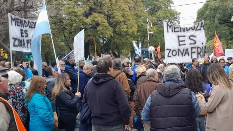 La imagen muestra una masiva movilización de jubilados, sindicatos y organizaciones sociales en la provincia de Mendoza, Argentina, en la que se despliegan carteles con la leyenda "Mendoza es zona fría" para manifestarse en defensa de los subsidios a las tarifas de gas.