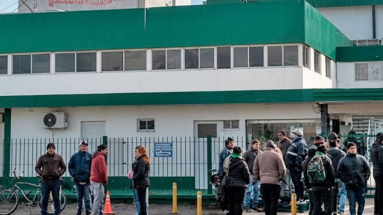 La imagen muestra a un grupo de trabajadores reunidos frente a la planta industrial de Granja Tres Arroyos en Capitán Sarmiento, provincia de Buenos Aires, en medio de la protesta y el conflicto por suspensiones y despidos.
