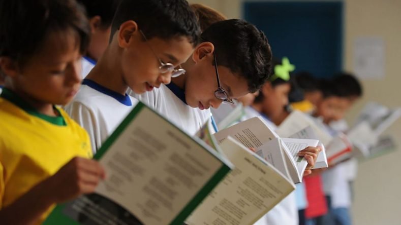 Esta imagen muestra a un grupo de jóvenes estudiantes concentrados en la lectura de libros dentro de un aula escolar.