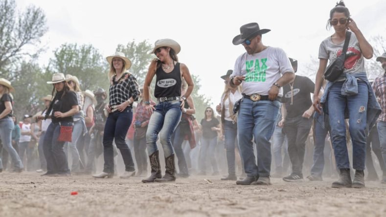 Esta imagen muestra a un grupo de personas bailando música country al aire libre, un estilo de baile conocido como line dance, presumiblemente en el San Pedro Country Music Festival en la Provincia de Buenos Aires.