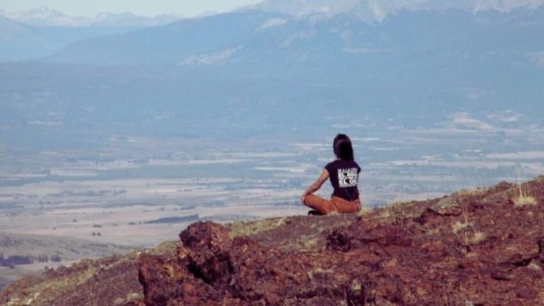 Esta imagen muestra una vista panorámica de un paisaje montañoso con una persona sentada en primer plano.