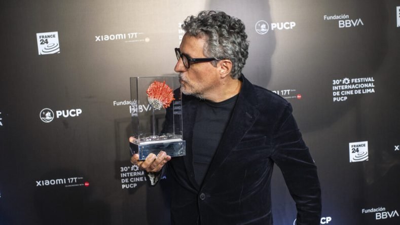 Esta imagen muestra al reconocido director de cine brasileño Kleber Mendonça Filho sosteniendo un galardón en un evento cinematográfico.