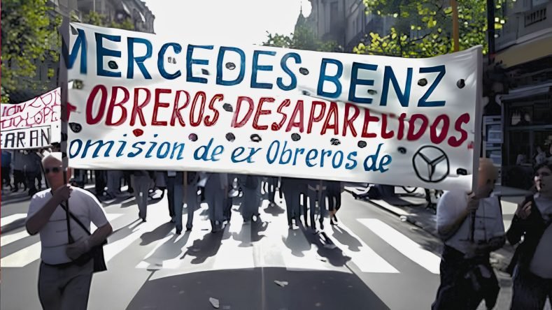 La imagen muestra una manifestación en Argentina con una gran pancarta que reclama por los obreros desaparecidos de la empresa Mercedes-Benz.
