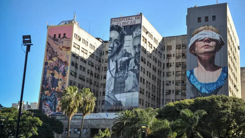 La imagen muestra la fachada del Hospital de Clínicas José de San Martín en Buenos Aires, decorada con tres murales gigantes que homenajean a las víctimas del atentado a la AMIA.
